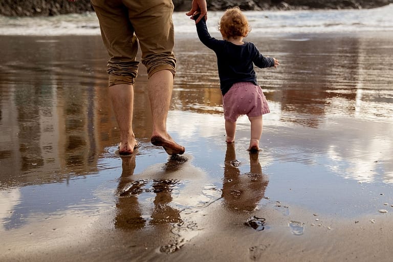 Man holding the hand of a young child while walking barefoot on the beach